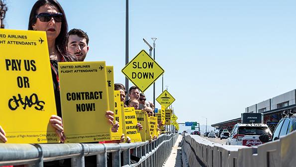 United Airlines flight attendants holding up yellow signs reading "pay us or chaos" and "contract now"