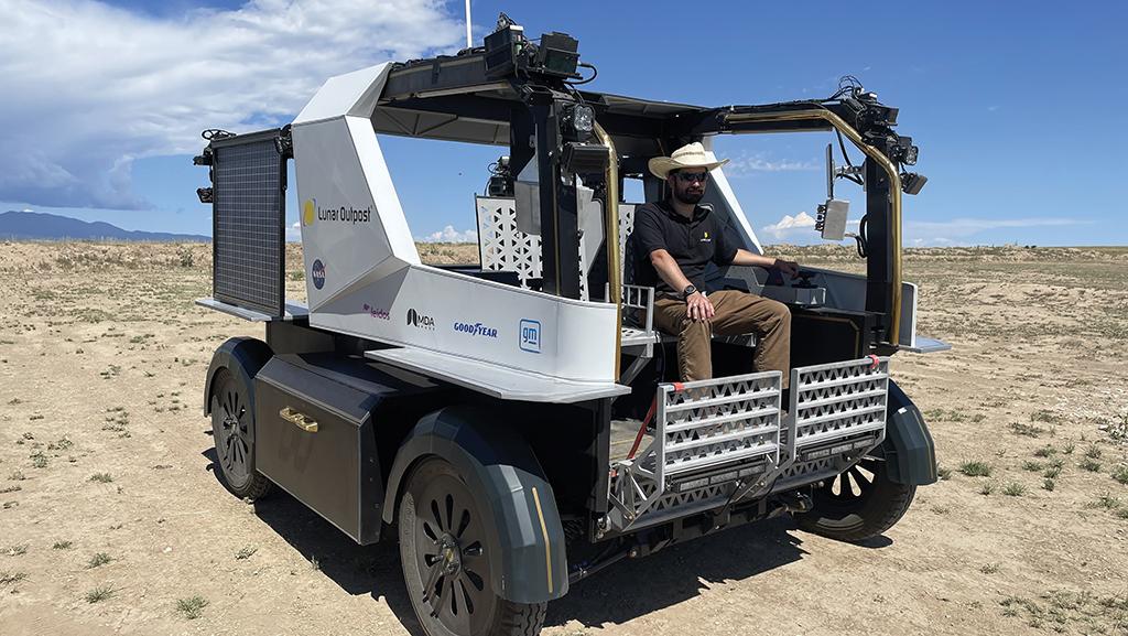 Man sitting in Lunar Outpost rover amid desert shrubland