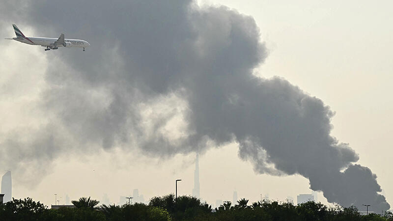 Emirates jet flying low with smoke plume in background