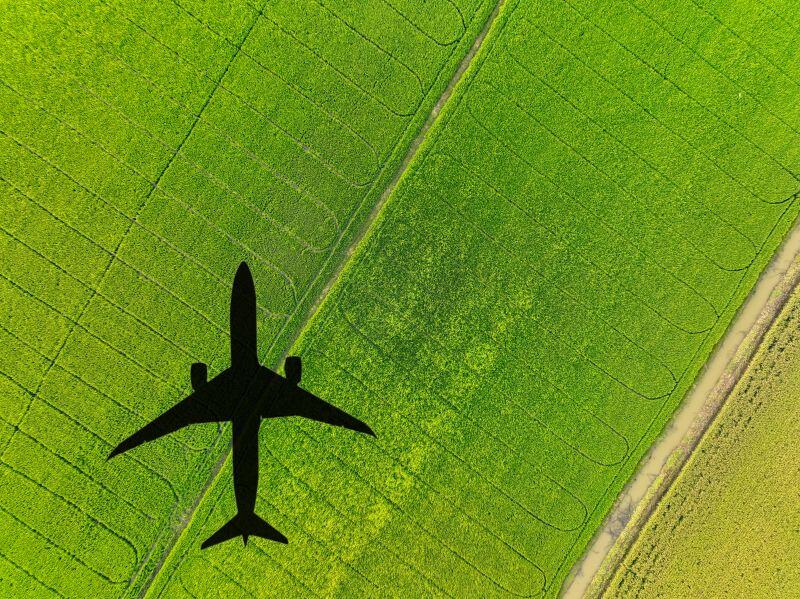 Aircraft flying with shadow over green grass 