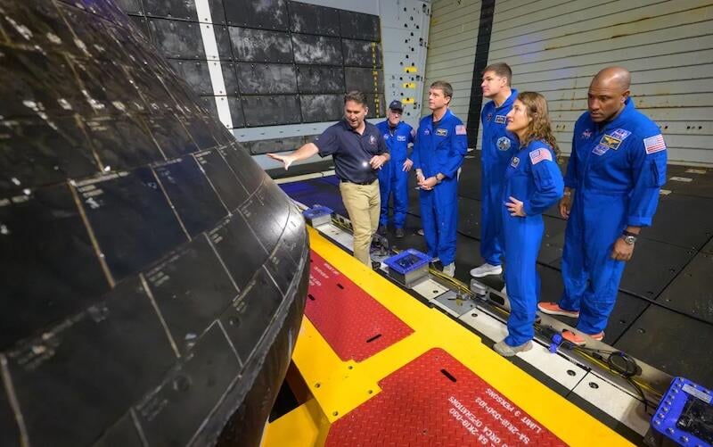 The crew of Artemis II inspect the outside of the Orion spacecraft in the well deck of the recovery vessel USS John P. Murtha, the day after their April 10 splashdown in the Pacific.