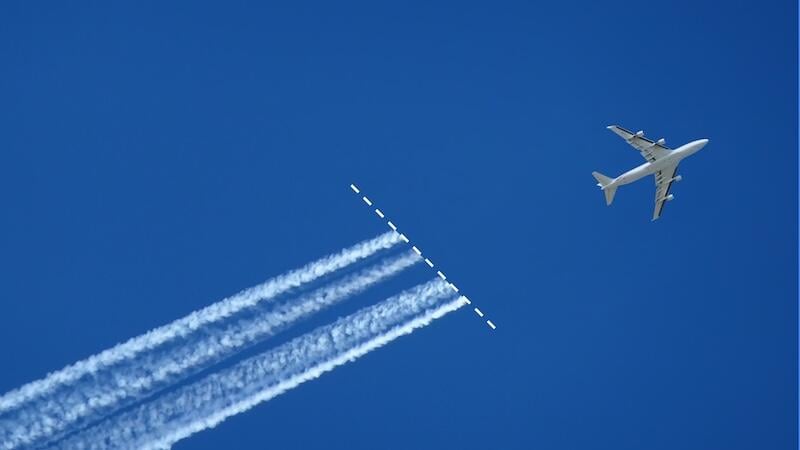 aircraft flying across blue sky above contrails
