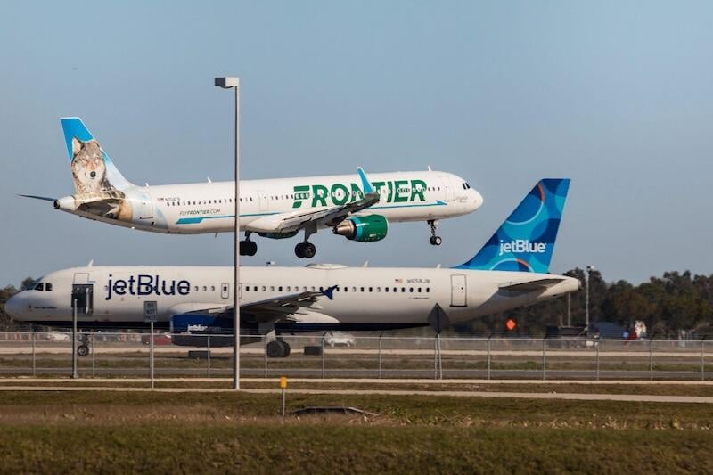 a frontier airlines plane lifts off above a parked jetblue aircraft