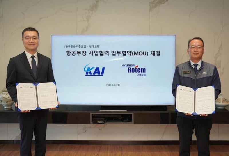 two executives hold signed documents beside screen announcing KAI–Hyundai partnership