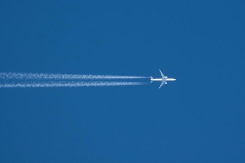 passenger aircraft flies across blue sky leaving contrails behind