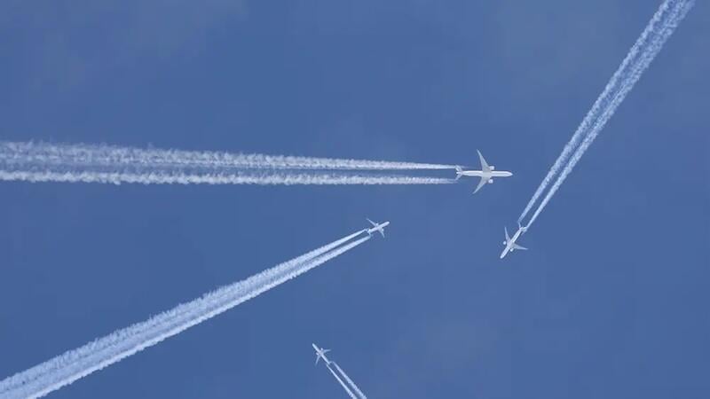 four aircraft in flight leaving white contrails across a clear blue sky
