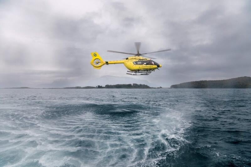 yellow helicopter hovers low above choppy ocean water