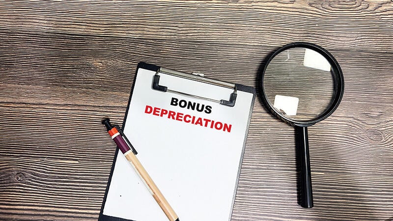 magnifying glass next to paper on clipboard that says BONUS DEPRECIATION
