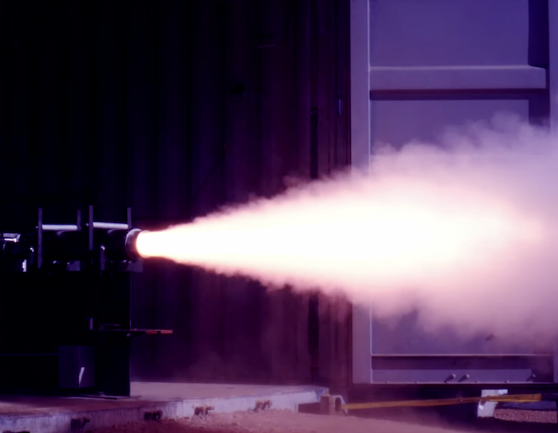 rocket engine fires white plume across a dark test chamber