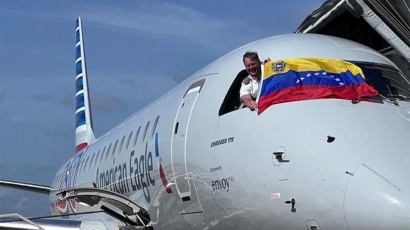 pilot with Venezuelan flag leaning out of american airlines aircraft cockpit window