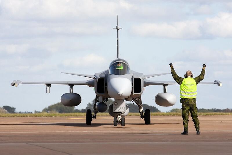 ground crew member in vest guides jas 39 gripen fighter jet
