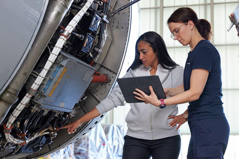 Technicians examine engine while consulting a tablet