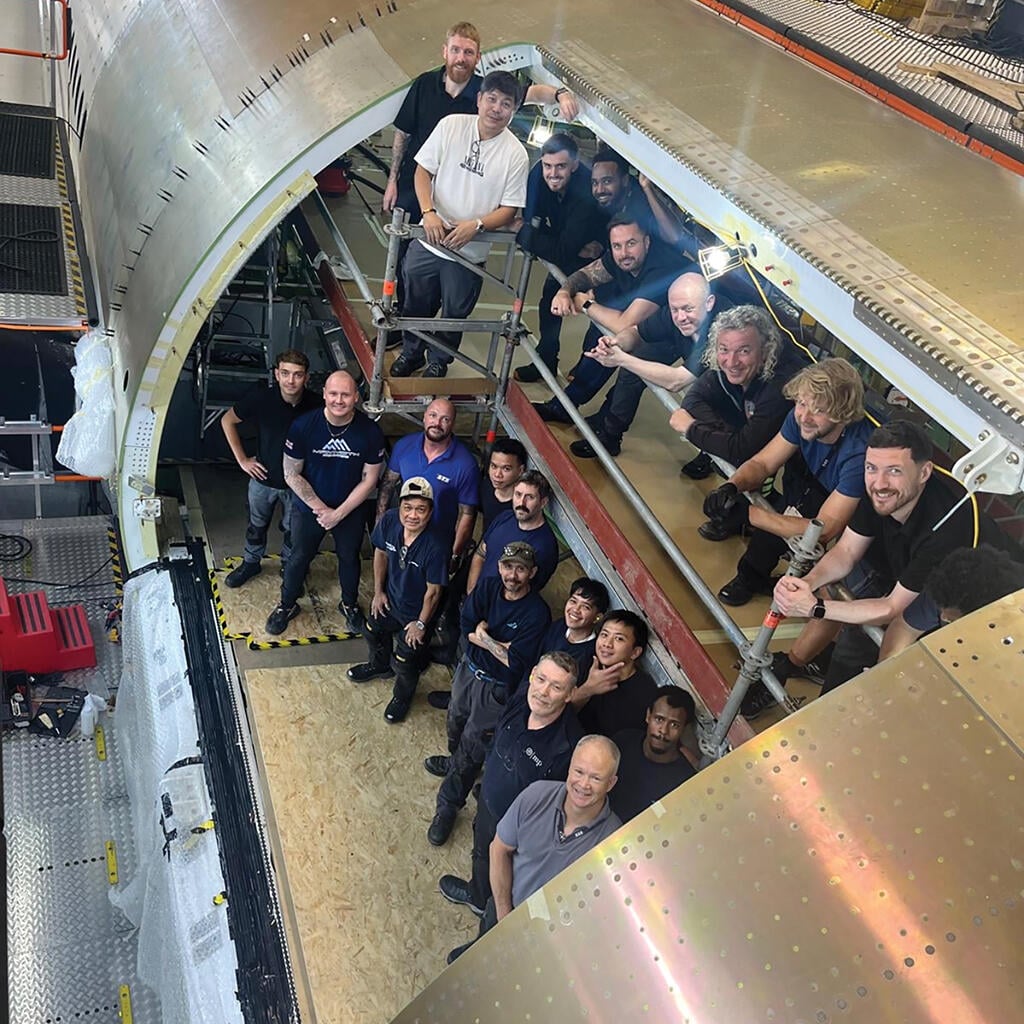 around 20 mechanics standing inside aircraft undergoing maintenance