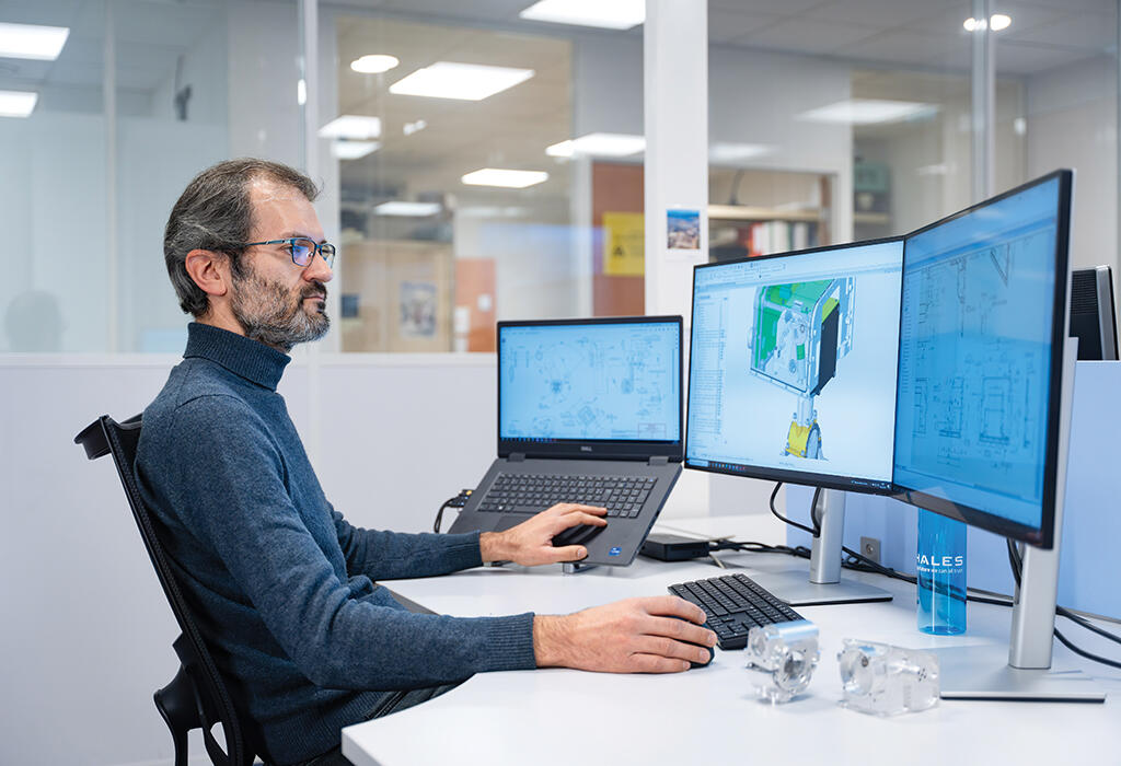 person sitting at desk with one laptop and two monitors