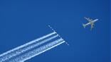 aircraft flying across blue sky above contrails