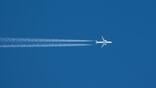 passenger aircraft flies across blue sky leaving contrails behind