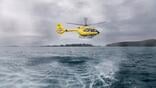 yellow helicopter hovers low above choppy ocean water