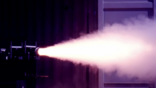 rocket engine fires white plume across a dark test chamber
