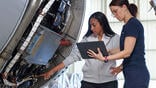 Technicians examine engine while consulting a tablet