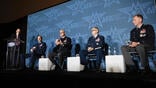 four U.S. military officers in chairs next to suited man by podium at conference