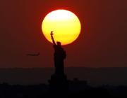sunset behind the statue of liberty with an airplane in the sky
