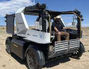 Man sitting in Lunar Outpost rover amid desert shrubland