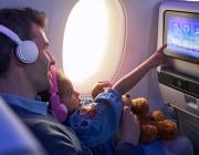 parent and child sitting on aircraft with inflight entertainment screen lit