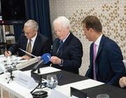 Bill Franke (second from left) reading from paper before news microphones