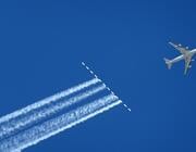 aircraft flying across blue sky above contrails