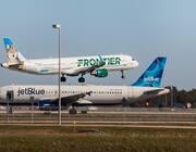a frontier airlines plane lifts off above a parked jetblue aircraft