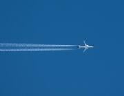 passenger aircraft flies across blue sky leaving contrails behind