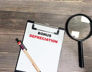 magnifying glass next to paper on clipboard that says BONUS DEPRECIATION