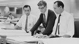 black-and-white photo of three engineers looking over drafting paper