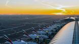 Dubai International Airport at sunset with a series of aircraft docked at a terminal.